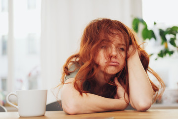 Red-haired girl sitting at table with boring face