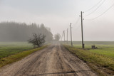 Fototapeta Tęcza - empty country gravel road with mud puddles and bumps