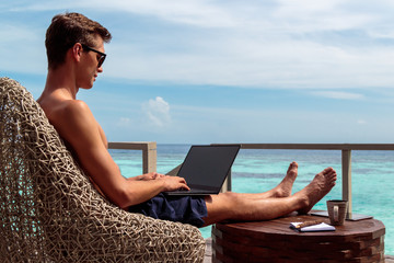 young man in swimsuit working on a laptop in a tropical destination