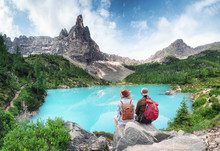 Travelers Couple Look At The Mountain Lake. Travel And Active Life Concept With Team. Adventure And Travel In The Mountains Region In Dolomite Alps, Italy