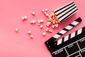 Film watching concept. Clapperboard and popcorn on pink background top view copy space