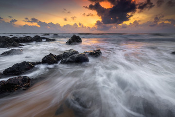 A scenery of sunrise with amazing unique rock formation and beautiful  flow of wave at Kemasik beach, Terangganu Malaysia. Soft focus during long exposure shot.