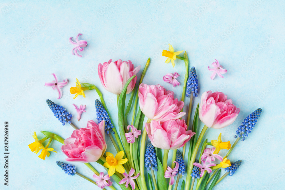 Bouquet of beautiful spring flowers on pastel blue table top view. Greeting card for International Women Day. Flat lay. - obrazy, fototapety, plakaty 