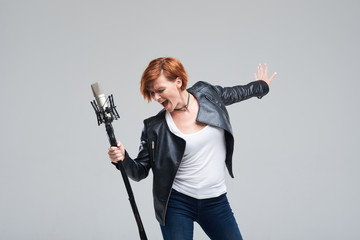 Wall Mural - Portrait of rock singer wearing leather jacket and keeping static mic, sings a song loudly on grey background. Concept of rock music and rave