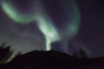 northern lights in norway in green, blue and violet colours and a silhouette of a mountains in front