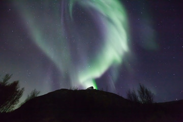 northern lights in norway in green, blue and violet colours and a silhouette of a mountains in front