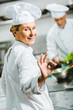 © LIGHTFIELD STUDIOS - beautiful smiling female chef in uniform and hat looking at camera and showing ok sign in restaurant kitchen