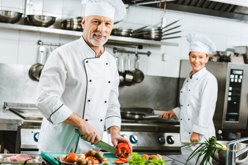 selective focus of male and female chefs in uniform preparing food in restaurant kitchen