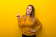 Young woman on yellow background showing and lifting a finger in sign of the best
