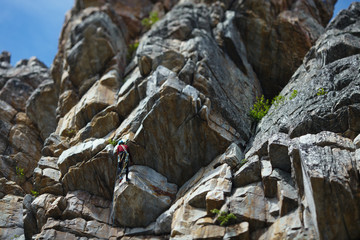 Wall Mural - The climber climbs up the rope against the background of a huge rock wall. Tilt-Shift effect.