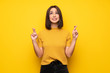 © luismolinero - Young woman over yellow wall with fingers crossing and wishing the best