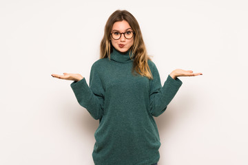 Teenager girl over white wall having doubts while raising hands and shoulders