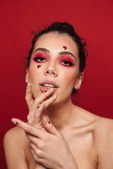 Poster - Woman with red bright makeup isolated over red wall background posing with hearts on face.