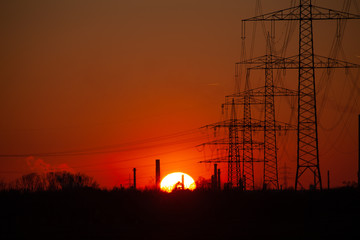 warm sunset with rim sun, industry and electricity masts with wires in fron of the red sky