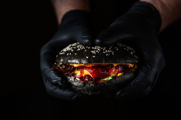 Close up of hands holding black juicy burger with cranberry sauce on dark background