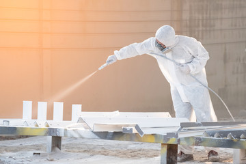 worker painting a mechanical part with airless spray