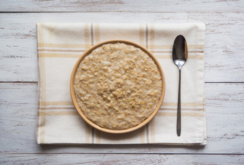 Oatmeal in a plate on a white wooden table.