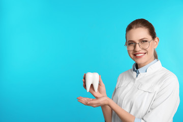 Canvas Print - Female dentist holding tooth model on color background. Space for text