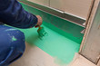 Worker is painting by brush with green colored waterproof finish material the bathroom floor in apartment is inder construction, remodeling, renovation, overhaul, extension, restoration and