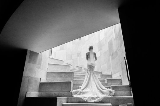 stylish bride posing on stairs at hotel. back view. beautiful woman in luxury white dress, bridal gown. creative black white photo