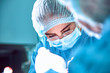 © Georgii - Close up portrait of young female surgeon doctor wearing protective mask and hat during the operation. Healthcare, medical education, surgery concept