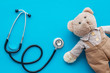 Children's doctor concept. Teddy bear toy and stethoscope on blue background top view space for text