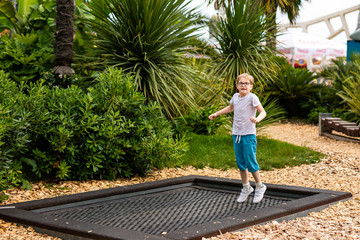 Blonde boy with glasses 7 years old jumping in the children playground in the entertainment park