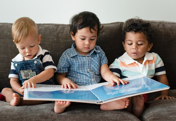 three little boys reading a book on a sofa