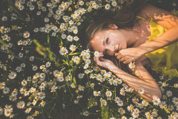 Portrait of young  woman with radiant clean skin lying down amid flowers on a lovely meadow on a spring/summer day