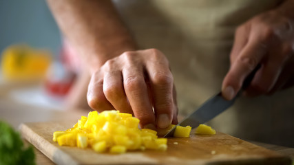 Mature husband cooking vegetable salad, cutting yellow pepper, culinary show