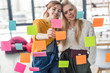© LIGHTFIELD STUDIOS - beautiful casual businesswomen colorful putting sticky notes on glass window in office