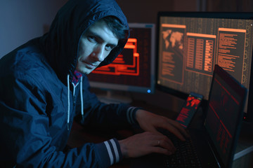 Wall Mural - Male in the hood looking in the camera. Hacker attacks and online fraud in the dark on the screen background in neon