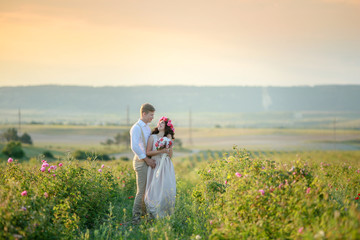 Wall Mural - The girl in the hands holding a gift, a bouquet of flowers, from roses.  Against a beautiful landscape. Happy young couple newlyweds, romantic family. walking at sunset in a wheat field.