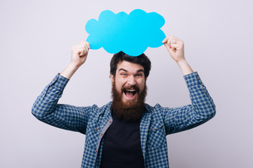 Wall Mural - Happy excited bearded  man holding up a speech cloud icon against copy space over white background