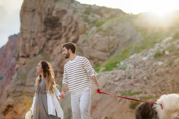 Romantic atmosphere. Happy couple woman and man walking the dog near the sea with mountains in the background.