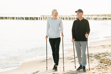 Nordic walking - senior man and pretty young girl working out on beach. Healthy lifestyle. Candid photo of father and daughter.