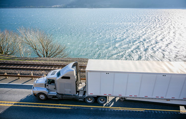 Gray big rig American bonnet semi truck with dry van semi trailer runing with cargo on the road along the Columbia River