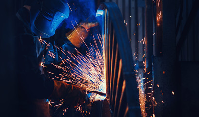 Professional welder performs welding work on metal in protective mask. Industrial worker concept