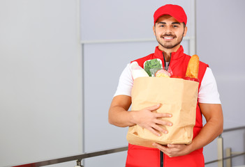 Canvas Print - Food delivery courier holding paper bag with products indoors. Space for text