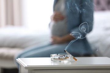 Poster - Cigarettes in ash tray and blurred pregnant woman on background, closeup. Space for text