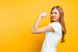 Leinwandbild Motiv of happy girl in white t-shirt showing arm muscles on yellow background.