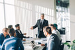 © alfa27 - Multiracial male business executives discussing project sitting at conference table in spacious hall with panoramic city scapes, all men dressed in formalwear and have positive mood