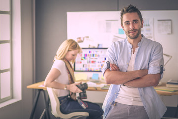 Poster - Portrait of young designer in front of laptop and computer while working. Assistant using her mobile at background.