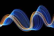 Long Exposure, Light Painting Photography.  Electric Blue And Vibrant Metallic Gold Colour, Waves And Swirls, Parallel Lines Pattern Of Movement, Against A Clean Black Background