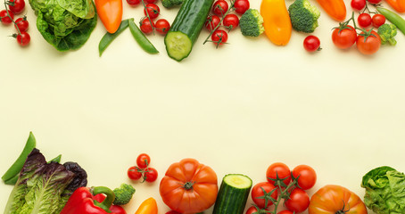 Raw vegetables background, tomatoes cucumbers lettuce pepper spring onion broccoli peas on light yellow table, top view, copy space, selective focus