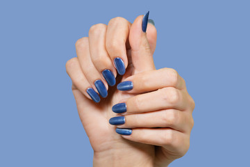 Closeup view of beautiful female hands with blue glossy professional manicure with cat eye effect. Horizontal color photography.