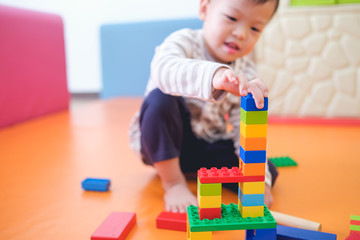 Cute little Asian 2 - 3 years old toddler boy child having fun playing with colorful plastic blocks indoor at play school / nursery / living room, Educational toys for young children concept