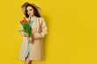 © maxbelchenko - Fashion photo of a beautiful young woman with tulips in her hand .she dressed in a beautiful coat,  and T-shirt with stripes on the yellow background .Spring concept. March 8. beautiful girl.