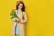 © maxbelchenko - Fashion photo of a beautiful young woman with tulips in her hand .she dressed in a beautiful coat,  and T-shirt with stripes on the yellow background .Spring concept. March 8. beautiful girl.