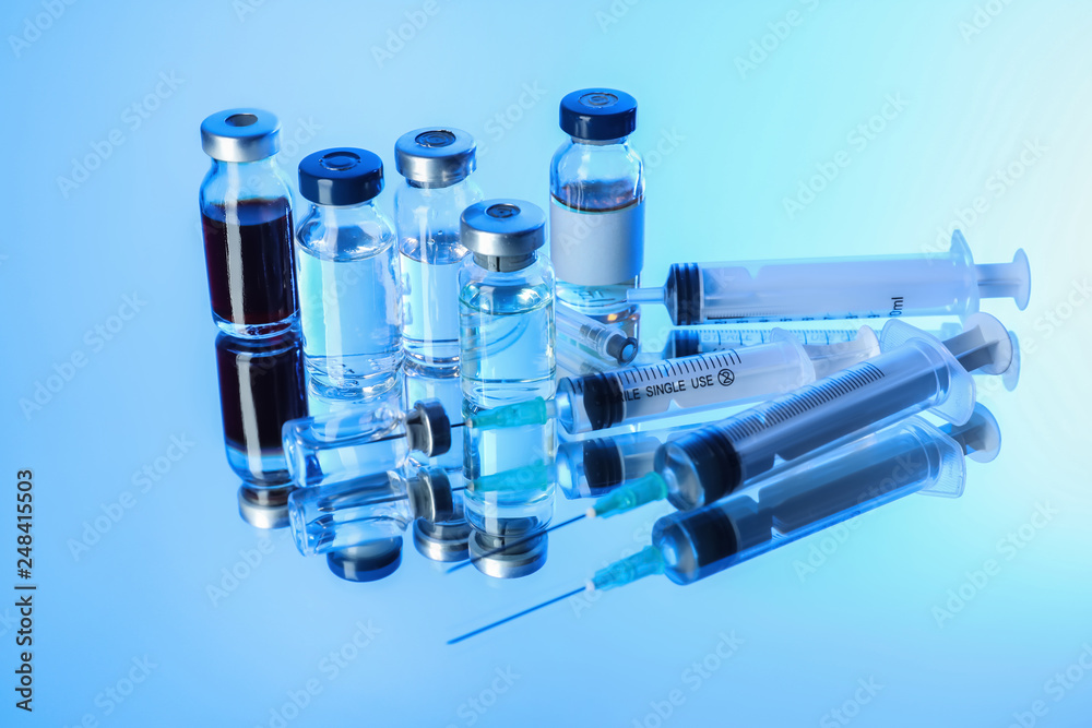 Syringes and ampules with vaccine against flu on color background
